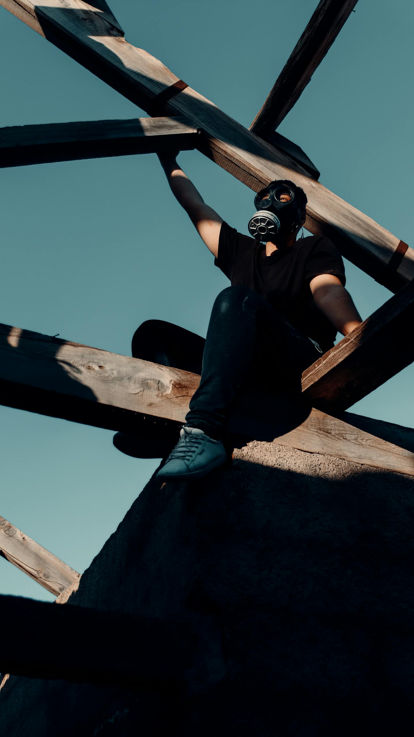 Man with Gas Mask Sitting on Wooden Beams of Roof Frame